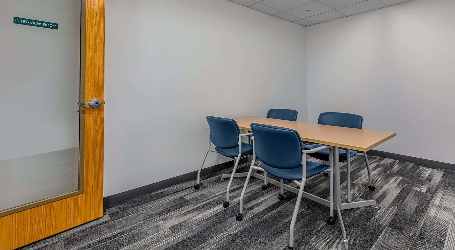 Interview room at the Aurora Police Department Headquarters. In the center of the room there is a wooden table with four chairs around it.
