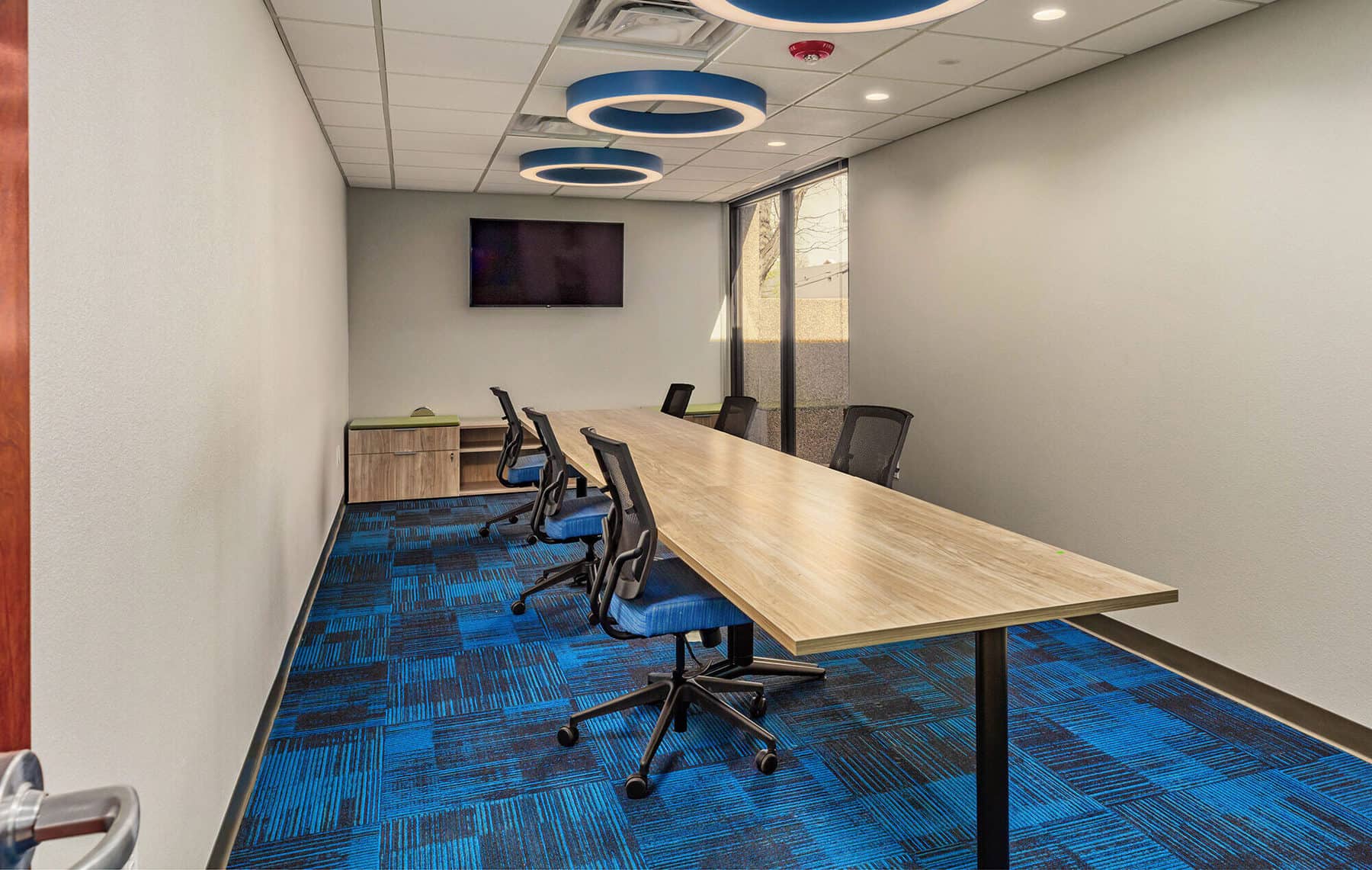Conference room with a long table in the middle with chairs surrounding. Modern lighting accents the modern design.