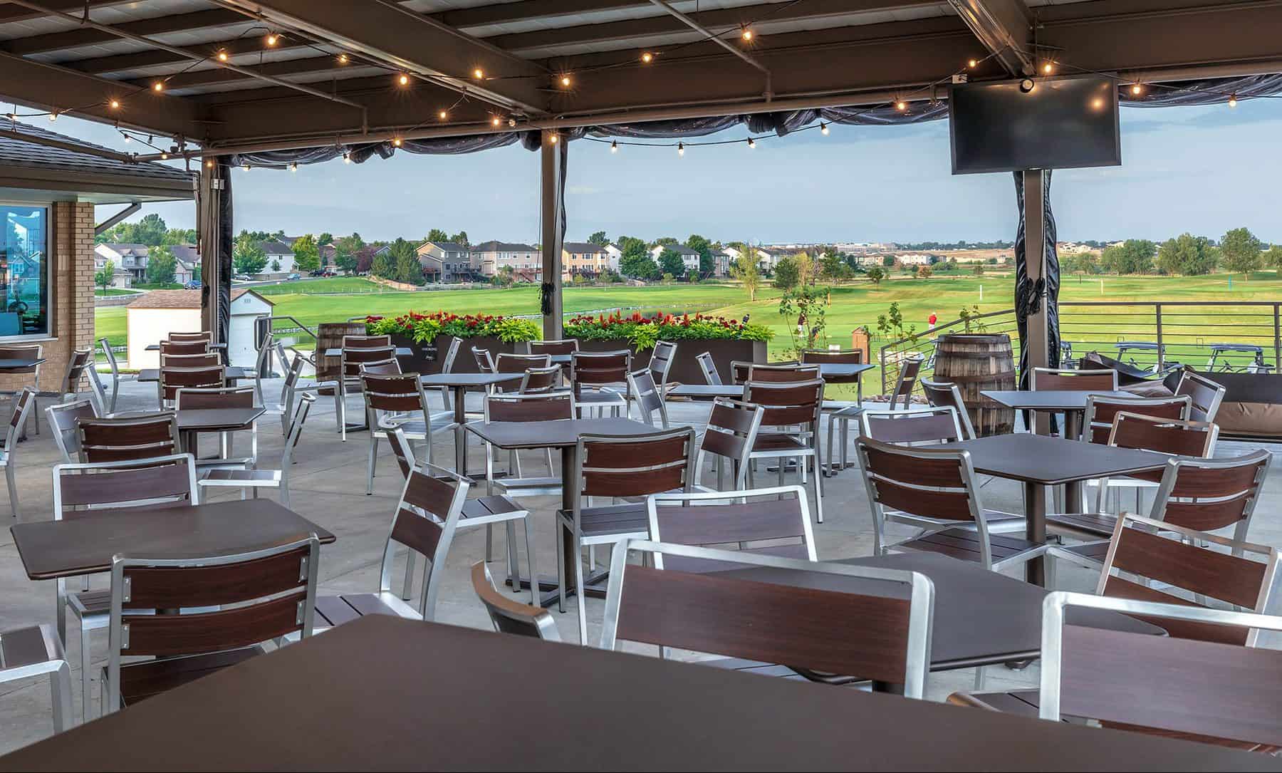 The outdoor patio section of the Thorncreek Golf Clubhouse. Chairs and tables cover a large area all under the outdoor covering with lights hanging from the ceiling.