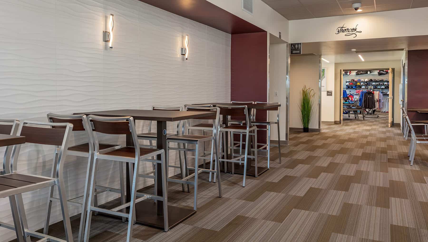 The interior entry of the Thorncreek golf clubhouse after remodeled, high tables and chairs against the wall to enjoy the indoors, have a bite to eat or a cold drink before or after a game of golf. Can see the retail shop at the end of the hallway.