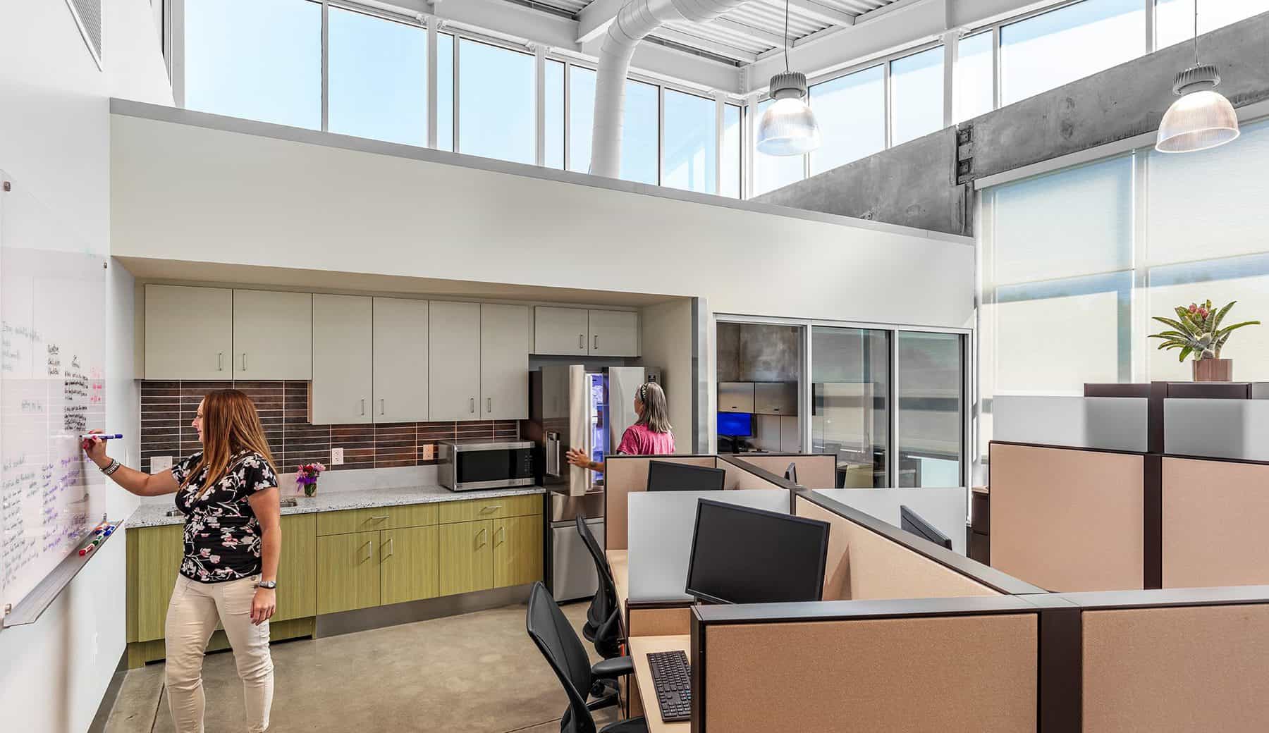 Office space well lit with natural lighting. A woman is drawing on a dry erase board.